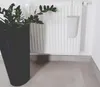 A black planter with a green plant is placed next to a white radiator with a white water evaporator hanging on it. Produktbild-Vorschau