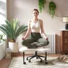 A woman meditates on a chair in a room with plants and a radiator. Produktbild-Vorschau