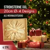 A straw star ornament is displayed in a box next to wrapped Christmas presents and a decorated Christmas tree. Produktbild-Vorschau