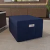 A dark blue ottoman is placed on a light gray carpet in a room with a wooden cabinet and a television in the background. Produktbild-Vorschau