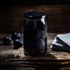 A jar of plums sits on a wooden surface next to a folded cloth. Podgląd zdjęcia produktu