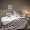 A neatly made bed with grey and white bedding, set against a neutral-toned wall. Produktbild-Vorschau