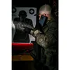 A person in tactical gear is on a phone call next to a shooting target. Produktbild-Vorschau