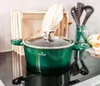 A green pot with a glass lid sits on a black induction stovetop, with a wooden crate and kitchen utensils in the background. Produktbild-Vorschau