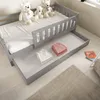 A children's bed with a pull-out drawer, featuring teddy bears and folded clothes. Produktbild-Vorschau