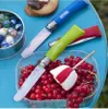 Three Opinel knives are displayed on a blue table with a container of red currants, a marshmallow on a stick, and a tin of marbles. Produktbild-Vorschau