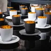 A collection of black and white espresso cups with gold interiors, arranged on a reflective black surface. Náhled obrázku produktu