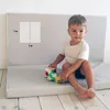A young child is sitting on a folded mat and playing with toys. Anteprima dell’immagine prodotto