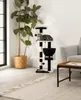 A cat is resting on a cat tree next to a large potted plant in a living room. Produktbild-Vorschau