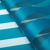 A close-up, angled view of a rolled-up fabric blind with horizontal stripes of blue and white. Produktbild-Vorschau
