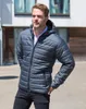 A man wearing a padded jacket and jeans stands outside a modern building. Produktbild-Vorschau