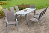An outdoor dining set with a table and chairs on a gravel surface with a lawn and flowerbed in the background. Produktbild-Vorschau