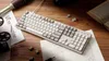 A mechanical keyboard is placed on a wooden desk next to an open book and a vintage telescope. Produktbild-Vorschau