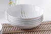 A stack of white bowls with floral designs on a bamboo mat. Anteprima dell’immagine prodotto