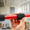 A hand holding a red telescopic pole with black grips in a construction or renovation site. Produktbild-Vorschau