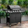 A black gas grill is shown outdoors on a wooden deck, with lush green plants in the background. Produktbild-Vorschau