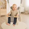 A baby is sitting in a gray swing in a nursery. There is a bookshelf and a dresser in the background. Náhled obrázku produktu