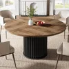 A round dining table with a wooden top and a fluted black base, surrounded by chairs in a dining room setting. Produktbild-Vorschau