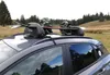 A ski and snowboard rack mounted on the roof of a car, parked in a grassy, wooded area. Produktbild-Vorschau