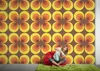 A young woman is sitting on a red beanbag chair in front of a wall with a retro circular pattern wallpaper. Produktbild-Vorschau