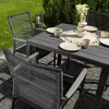 An outdoor dining set with chairs and a table, set on a patio with greenery in the background. Náhľad obrázku produktu
