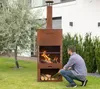 A man is tending to a fire in a rusty metal grill fireplace in a backyard setting. Voir les images du produit