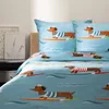 A bed with blue bedding featuring a pattern of dachshunds surfing on surfboards. Podgląd zdjęcia produktu