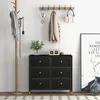 A hallway or entryway scene featuring a black dresser with gold accents, a wooden coat rack with a scarf and a light fixture, and a framed poster on the wall. Produktbild-Vorschau