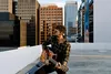 A man playing a guitar on a rooftop with city buildings in the background. Produktbild-Vorschau