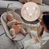 A baby is in a bouncer, with a woman sitting nearby. An inset shows a close-up of the bouncer's harness. Produktbild-Vorschau