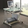 A computer desk with a monitor, keyboard, mouse, printer, and computer tower, placed near a large window with a view of greenery. Podgląd zdjęcia produktu