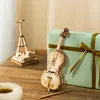A wooden model of a cello and a wooden model of the Eiffel Tower are displayed on a wooden table next to a light blue gift box with a gold ribbon. Anteprima dell’immagine prodotto