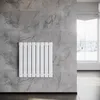 A white radiator is mounted on a gray tiled wall in a modern room with a window in the background. Podgląd zdjęcia produktu