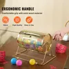 A hand is turning the crank of a golden lottery drum filled with colorful balls, set on a wooden table with tickets and smaller balls scattered around. Náhled obrázku produktu