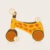 A yellow and orange giraffe-themed balance bike for children, with numbered callouts pointing to different parts of the bike. Anteprima dell’immagine prodotto