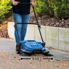 A person is using a blue and black push sweeper on a paved walkway with some debris. Náhľad obrázku produktu