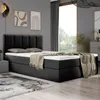 A bedroom scene featuring a black boxspring bed with a mattress and topper, a blanket draped over it, and decorative artwork on the wall. Produktbild-Vorschau