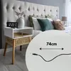 A bedside table with a digital clock and a woven drawer, next to a bed with pillows and a headboard. Produktbild-Vorschau