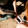 Two people pouring drinks from a green Stanley thermos into cups outdoors. Náhled obrázku produktu