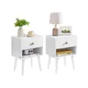 Two white nightstands with wooden legs and gold handles, each styled with decorative items like a lamp, books, and plants. Produktbild-Vorschau