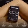 A black product box for OOONO CO-DRIVER NO1 is placed on a brown leather car seat. Produktbild-Vorschau