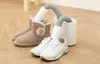 A shoe dryer with two nozzles, one inserted into a pair of white sneakers and the other into a pair of beige boots, placed on a wooden floor. Produktbild-Vorschau