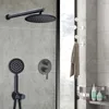 A black shower system mounted on a gray tiled wall, with a towel hanging on a rack to the right. Náhled obrázku produktu