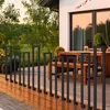A modern deck with a wooden floor and a black metal railing, leading to a house with a patio table and chairs. Náhľad obrázku produktu