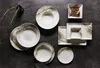 A collection of ceramic plates and bowls with a marbled design, arranged on a dark gray surface. Produktbild-Vorschau