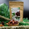 A bag of dried dates for parrots is displayed with some decorative elements like leaves and moss. Voir les images du produit