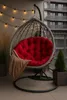 A hanging egg chair with a red cushion and a brown blanket on a balcony with string lights and plants. Produktbild-Vorschau