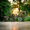 Three metal garden spheres of varying sizes sit on a wooden deck with a blurred background of trees and sunlight. Voir les images du produit