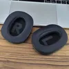Two black ear pads for headphones are placed on a wooden surface in front of a laptop. Náhled obrázku produktu