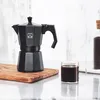 A black moka pot, a glass of coffee, and a jar of coffee beans are displayed on a countertop. Produktbild-Vorschau